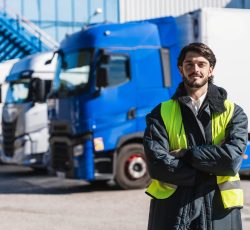 Professional truck driver in protective uniform standing confidently in front of semi trucks at a cold storage warehouse
